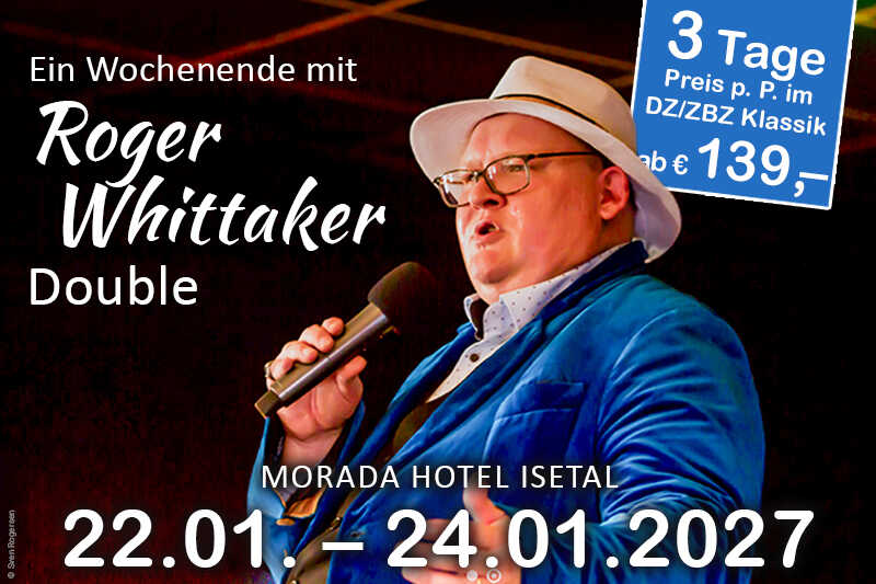Ein Sänger im blauen Sakko und weißen Hut steht mit Mikrofon auf der Bühne vor einem dunklen, stimmungsvoll beleuchteten Hintergrund.