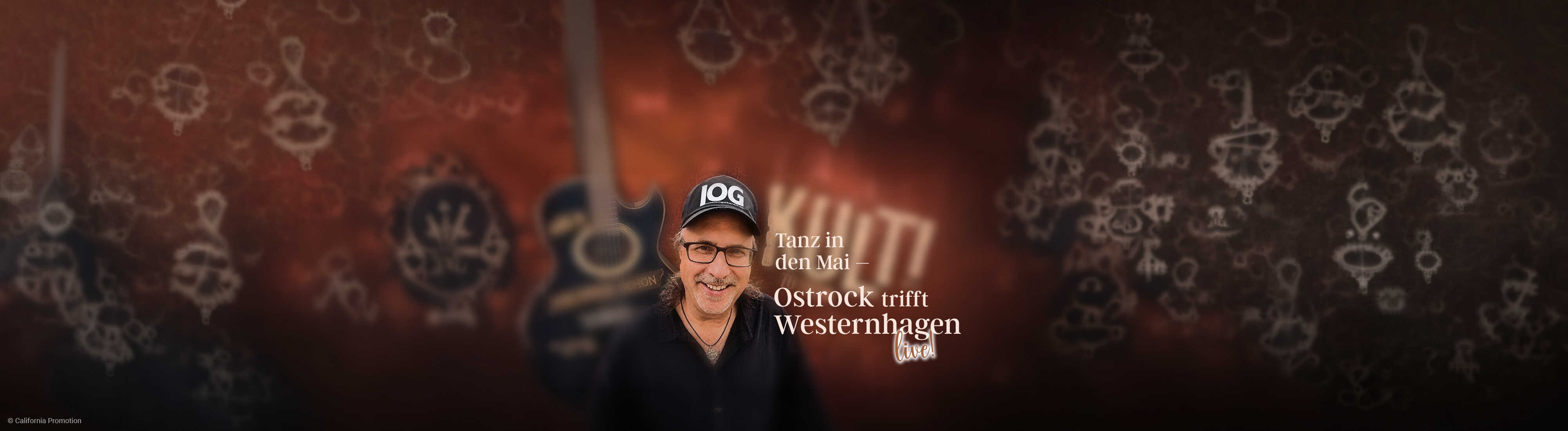 Ein lächelnder Musiker mit schwarzer Kappe und Brille steht vor warmem Hintergrund und kündigt einen stimmungsvollen Tanzabend mit Ostrock und Westernhagen-Musik an.
