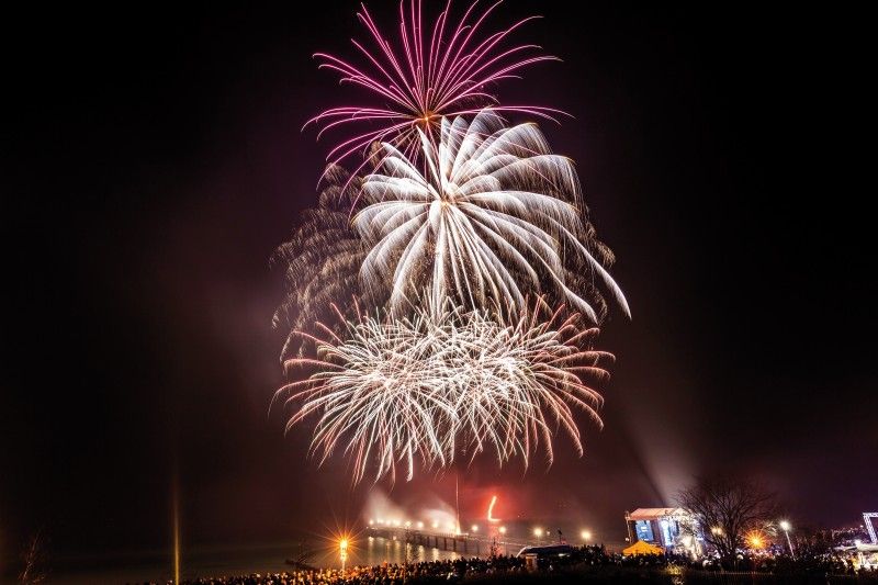 Farbenfrohes Feuerwerk am Nachthimmel über einem belebten Festplatz.