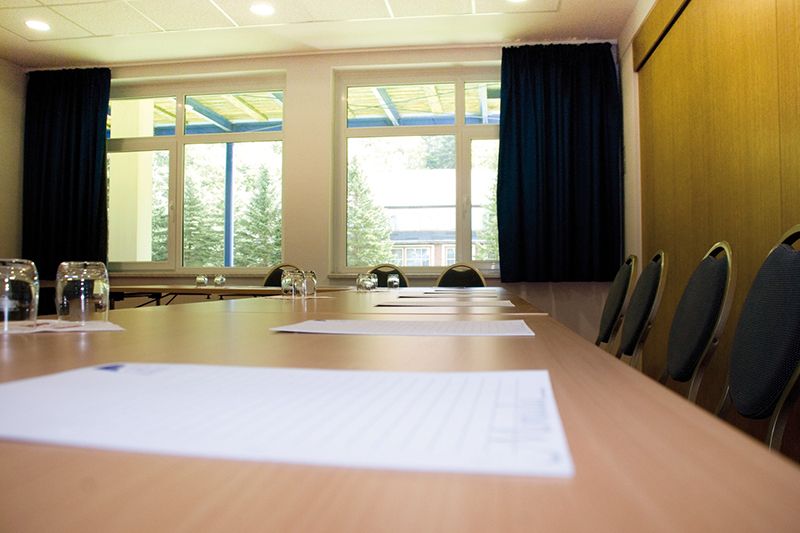 Leerer Konferenzraum mit großem Fenster, einem langen Tisch mit Stühlen und Dokumenten darauf.