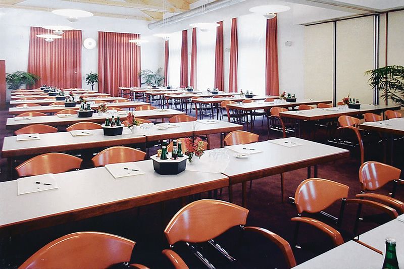 Konferenzraum mit gedeckten Tischen und roten Stühlen, dekoriert mit Pflanzen und Vorhängen