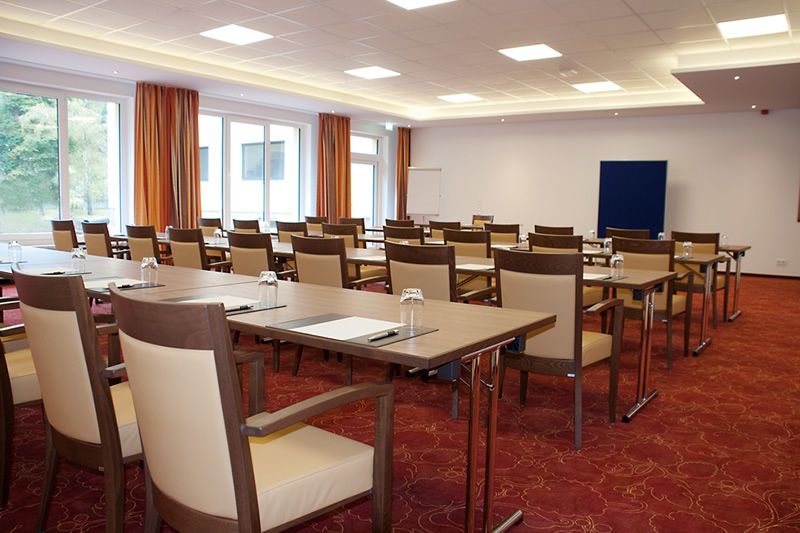 Konferenzraum mit langen Tischen und Stühlen, vorbereitet für ein Meeting mit Gläsern und Schreibmaterialien.