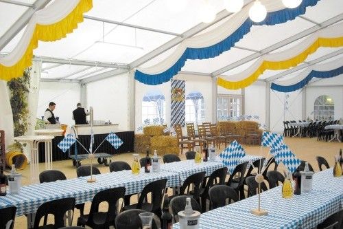 Festlich dekoriertes Veranstaltungszelt mit langen Tischen und bayerischen Fahnen, im Hintergrund zwei Personen bei der Vorbereitung.