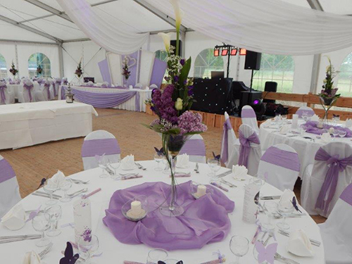 Elegantes festliches Zelt mit runden Tischen, geschmückt mit lila Stoffen und floralen Arrangements.