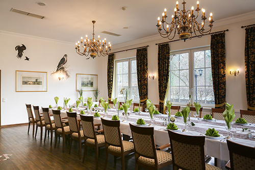 Eleganter Speisesaal mit einer langen, festlich gedeckten Tafel, zwei Kronleuchtern und großen Fenstern.