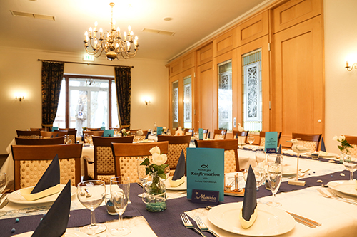 Ein festlich dekorierter Raum mit gedeckten Tischen für eine Konfirmationsfeier, inkl. Karten und blauer Deko.