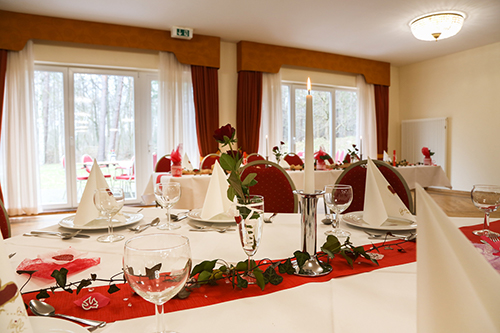 Eleganter Bankettsaal mit weiß gedeckten Tischen, dekoriert mit roten Rosen, Kerzen und Gläsern.