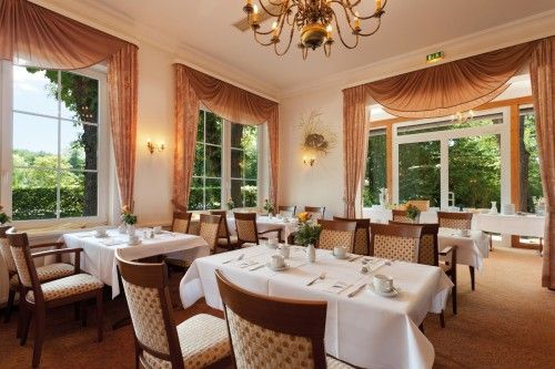 Elegantes Restaurant mit gedeckten Tischen, großen Fenstern und Kronleuchter.