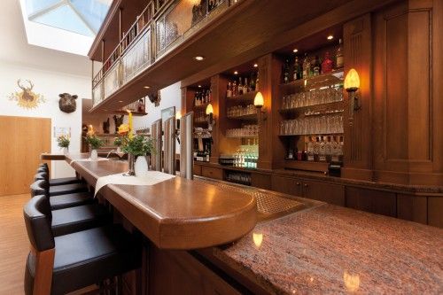 Innenansicht einer stilvollen Bar mit Holzausstattung, Lederbarhockern und dekorativen Pflanzen.