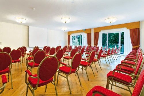 Konferenzraum mit roten Stühlen, einem großen Bildschirm und Fenstern mit Vorhängen