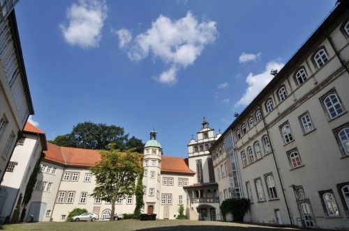 Innenhof eines historischen Gebäudes mit mehreren Flügeln und einem Turm unter blauem Himmel.