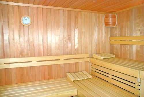 Leere, helle Sauna aus Holz mit Sitzbänken und einem Thermometer an der Wand