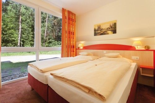 Helles Hotelzimmer mit zwei Einzelbetten und großem Fenster mit Blick auf einen Wald.