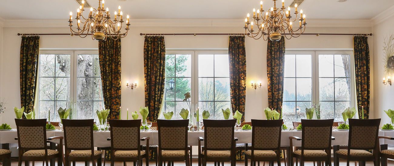 Eleganter Speisesaal mit großem Tisch, dekoriert mit Pflanzen, umgeben von hohen Fenstern und Kronleuchtern.