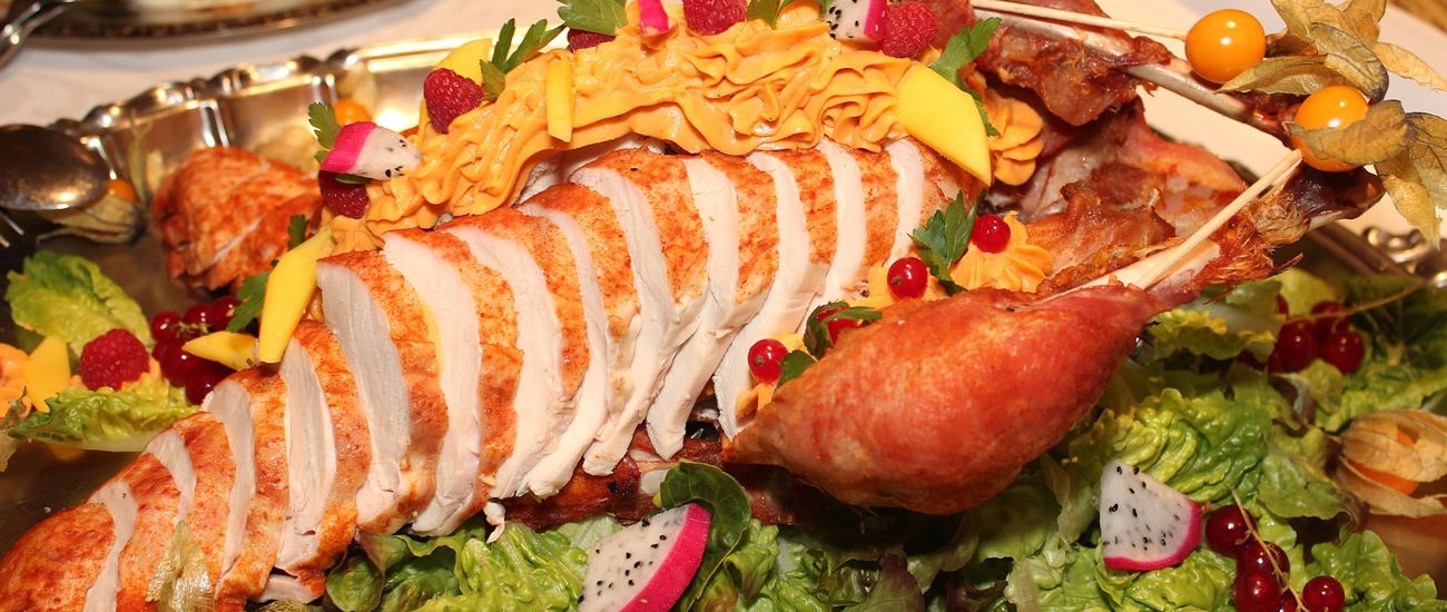 Präsentation eines kunstvoll angerichteten Truthahnbratens, umgeben von buntem Obst und Gemüse.